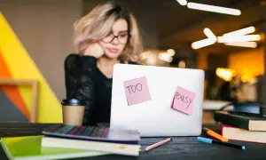 Kobieta z okularami przy laptopie, na którym karteczki "Too busy". Nawet przy natłoku obowiązków, samodzielna nauka angielskiego jest możliwa.