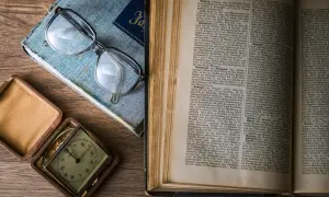 Otwarta księga rodzaju opracowanie, okulary i zabytkowy zegarek kieszonkowy na drewnianym stole.