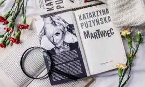 Książki Katarzyny Puzyńskiej, kwiaty i szkło powiększające na białym tle.