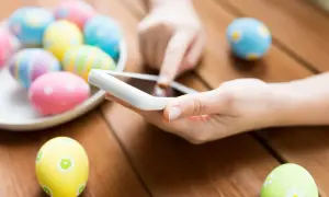 Kolorowe pisanki na drewnianym stole, a obok dłoń trzymająca smartfon, być może wysyłająca życzenia wielkanocne po rosyjsku.
