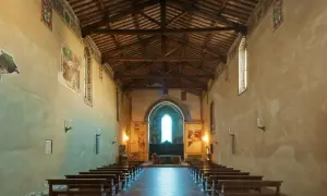 Wnętrze średniowiecznego kościoła z ławkami i freskami na ścianach.
