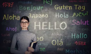 Kobieta w okularach przed tablicą z napisem "HELLO" i powitaniami w różnych językach. Czy to podpowiedź, jaki jest najtrudniejszy język w Europie?