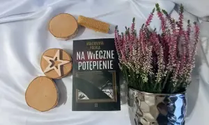 Książka "Na wieczne potępienie" Małgorzaty Rogali, wrzosy w ozdobnej doniczce, drewniane krążki i wafel.