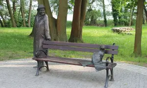 Pomnik mężczyzny w kapeluszu i kota na ławce w parku.