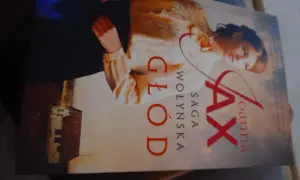 Okładka książki "Głód. Saga Wołyńska" Joanny Jax z portretem kobiety i budynkiem.