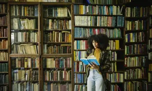 Kobieta z burzą włosów czyta książkę w bibliotece pełnej książek, jak w serii Lisy Gardner.