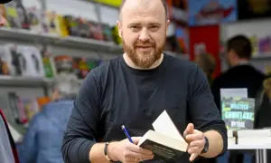 Chmielarz cykl gliwicki. Autor z książką i długopisem, w tle regały z publikacjami.