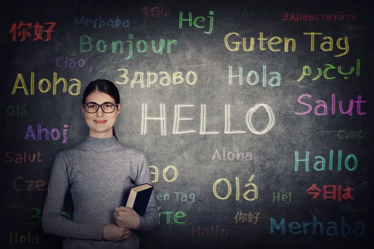 Kobieta w okularach przed tablicą z napisem "HELLO" i powitaniami w różnych językach. Czy to podpowiedź, jaki jest najtrudniejszy język w Europie?