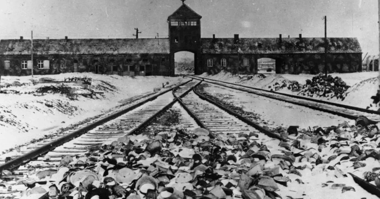 Brama obozowa Auschwitz, tory kolejowe, stosy porzuconych rzeczy. To obraz, który przypomina o tragedii.