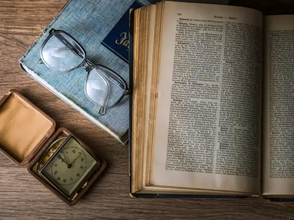Otwarta księga rodzaju opracowanie, okulary i zabytkowy zegarek kieszonkowy na drewnianym stole.