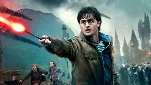 Harry Potter z różdżką w dłoni, w tle bitwa o Hogwart. To scena z serii filmowej Harry Potter.